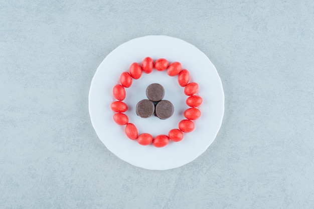 Um prato branco com doces vermelhos doces e biscoitos de chocolate no fundo branco. foto de alta qualidade