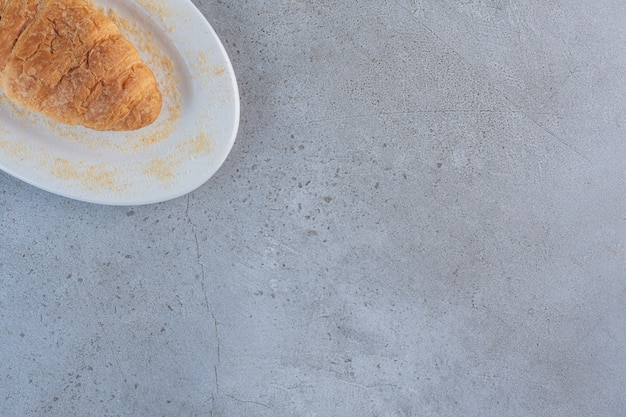 Um prato branco de delicioso croissant doce na mesa azul.