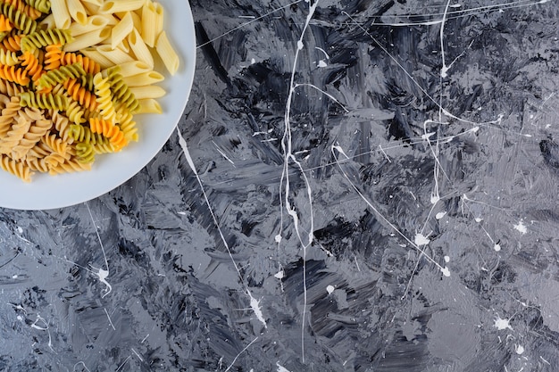 Um prato branco de massa Fusilli multicolorida crua e seca com macarrão Penne