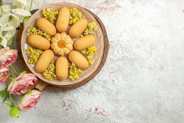 Um prato de biscoitos em uma travessa de madeira e flores no lado esquerdo do mármore