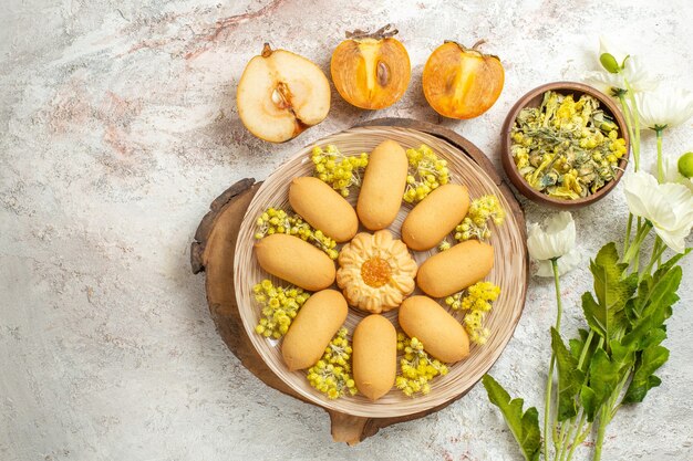 Um prato de biscoitos em uma travessa de madeira e uma tigela de ervas e meia pêra e palma e flores