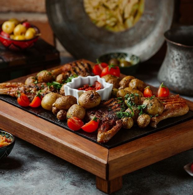 Um prato de carne grelhada, batatas e legumes em uma mesa de pedra