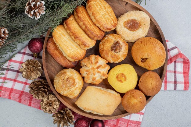 Um prato de madeira cheio de pastéis doces com bolas de natal e pinhas.