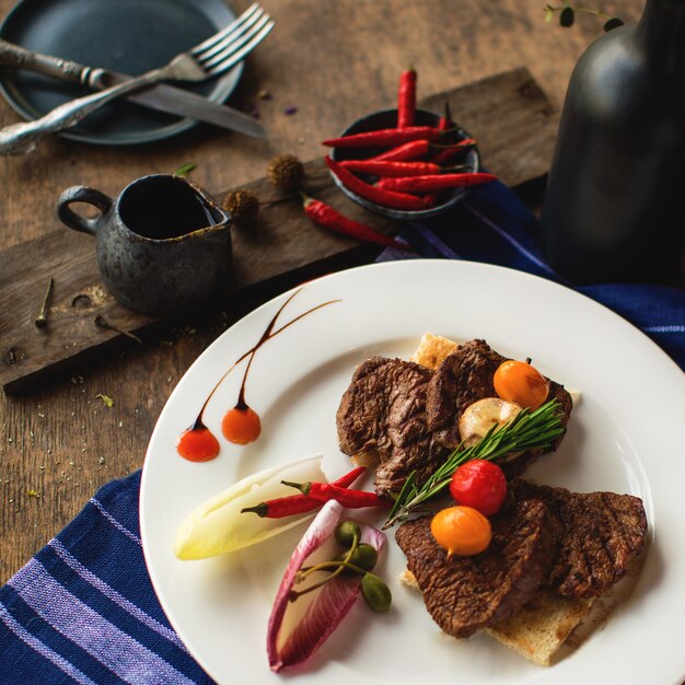 Um prato de pedaços de bife de cordeiro, guarnecido com legumes e alecrim