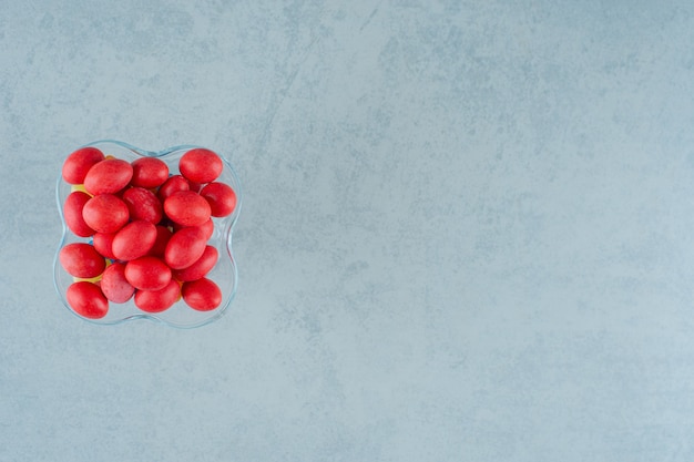 Um prato de vidro cheio de doces deliciosos doces vermelhos em uma superfície branca