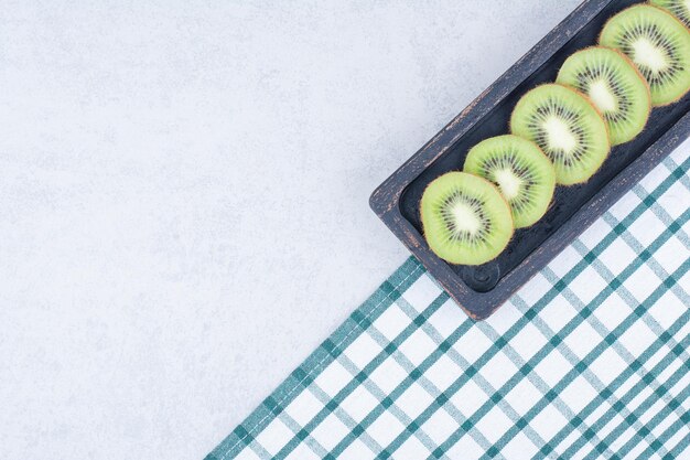 Um prato escuro de kiwi fresco fatiado na toalha de mesa.