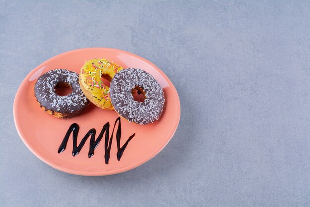 Um prato laranja de deliciosos donuts de chocolate com granulado.