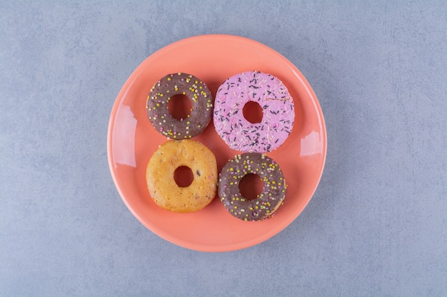 Um prato laranja de deliciosos donuts de chocolate com granulado.