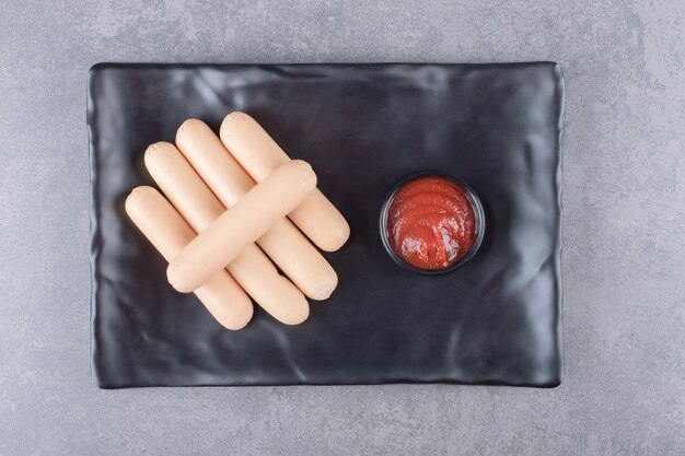 Um prato preto de salsichas cozidas com ketchup