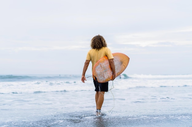 Um surfista entra no oceano com uma prancha pegando ondas.