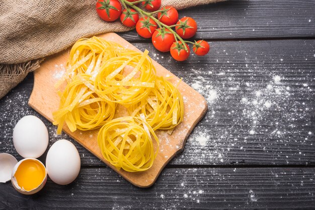 Um tomate orgânico; Tagliatelle cru com ovos quebrados e inteiros na mesa de madeira