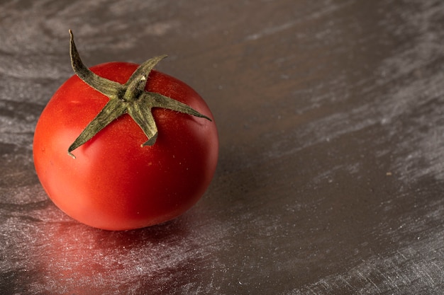 Um único tomate vermelho em um fundo metálico prateado.