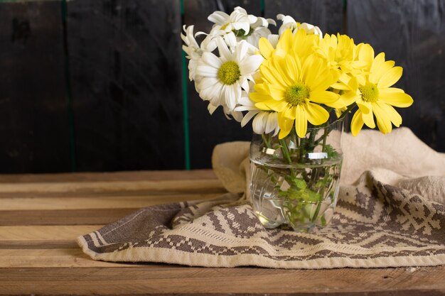 Um vaso de vidro de flores amarelas e brancas