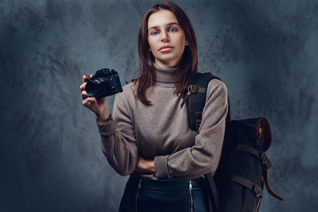 Um viajante feminino morena com mochila detém câmera fotográfica compacta.