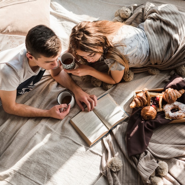 Um, visão aérea, de, par, encontrar-se cama, segurando, xícara café, livro leitura