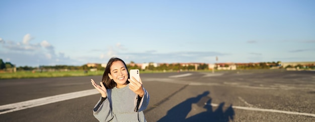 Uma adolescente asiática feliz tira selfie em bate-papo de vídeo em um aplicativo de smartphone enquanto está sentada em um patinador de skate