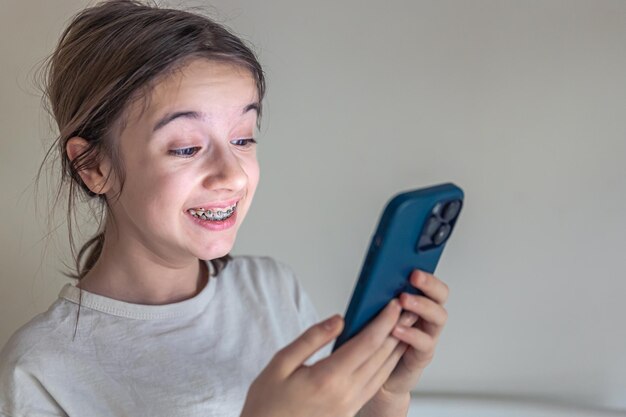 Uma adolescente com aparelho sorri e olha para a tela do smartphone