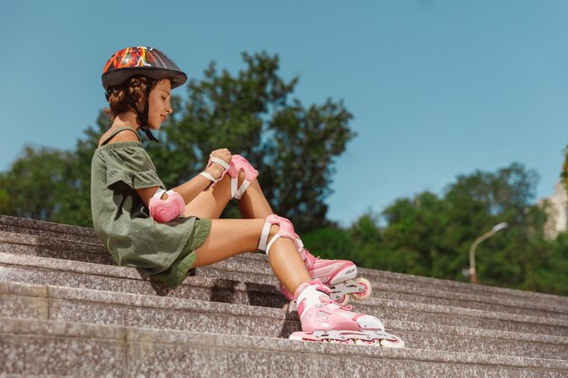 Uma adolescente de capacete aprende a andar de patins segurando o equilíbrio ou patinando e girando nas ruas da cidade em um dia ensolarado de verão