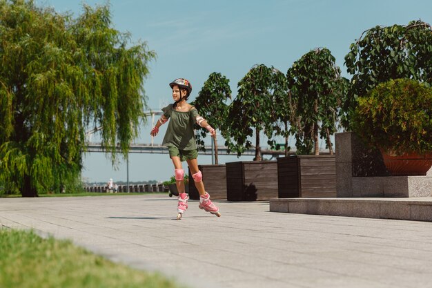 Uma adolescente de capacete aprende a andar de patins segurando o equilíbrio ou patinando e girando nas ruas da cidade em um dia ensolarado de verão