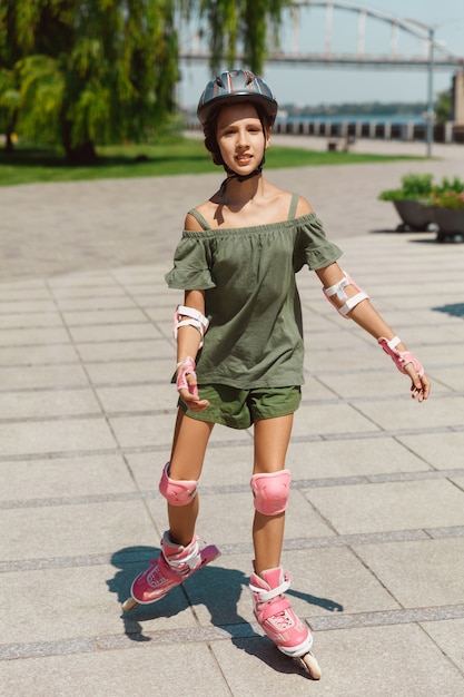 Uma adolescente de capacete aprende a andar de patins segurando o equilíbrio ou patinando e girando nas ruas da cidade em um dia ensolarado de verão