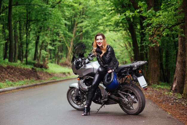 Uma atraente garota sexy vestida de couro posando perto de uma moto esportiva do lado de fora