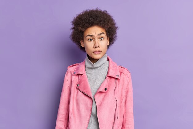 Uma bela jovem afro-americana perplexa com uma jaqueta rosa da moda reage a algo com uma expressão insatisfeita