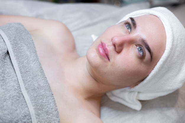 Uma bela jovem deita-se na mesa da esteticista e recebe procedimentos, uma leve massagem facial com óleo.