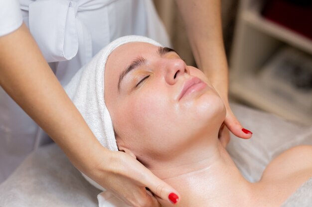 Uma bela jovem deita-se na mesa da esteticista e recebe procedimentos, uma leve massagem facial com óleo.