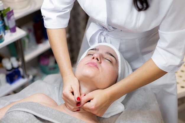 Uma bela jovem deita-se na mesa da esteticista e recebe procedimentos, uma leve massagem facial com óleo.