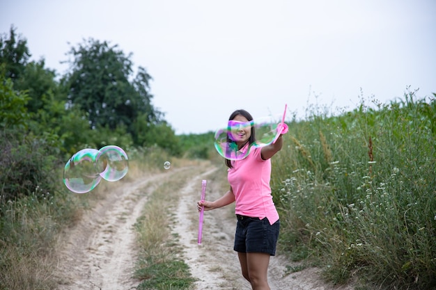 Uma bela jovem lança enormes bolhas de sabão no fundo bela natureza.