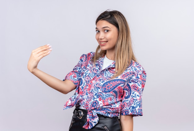 Uma bela jovem vestindo uma camisa com estampa paisley levantando a mão enquanto olha para uma parede branca