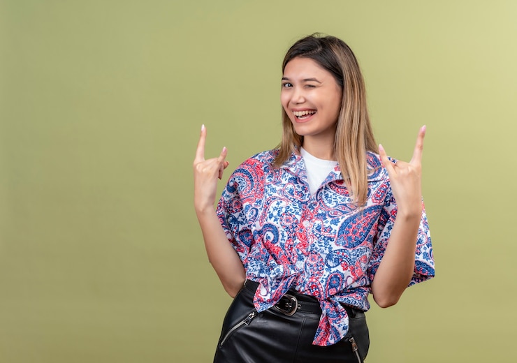 Foto grátis uma bela jovem vestindo uma camisa estampada de paisley mostrando um gesto de pedra com as mãos