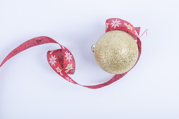 Uma bola dourada brilhante com fita vermelha de natal no branco