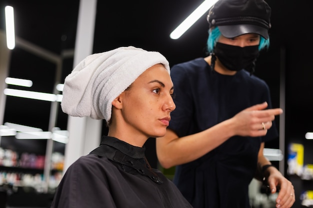 Uma cabeleireira profissional faz o corte de cabelo de um cliente. A menina está sentada com uma máscara no salão de beleza