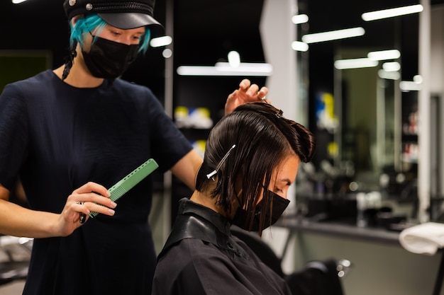 Uma cabeleireira profissional faz o corte de cabelo de um cliente. a menina está sentada com uma máscara no salão de beleza