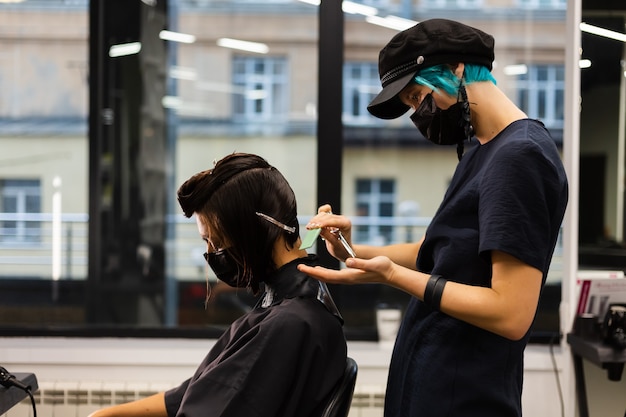 Uma cabeleireira profissional faz o corte de cabelo de um cliente. a menina está sentada com uma máscara no salão de beleza