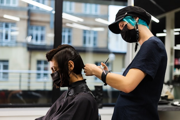 Uma cabeleireira profissional faz o corte de cabelo de um cliente. a menina está sentada com uma máscara no salão de beleza