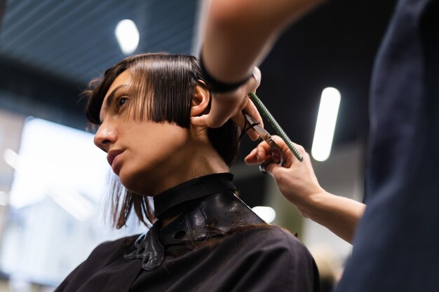 Uma cabeleireira profissional faz o corte de cabelo de um cliente. A menina está sentada com uma máscara no salão de beleza