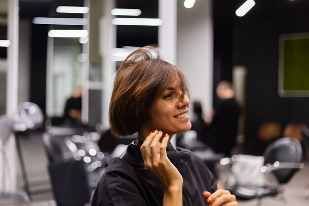 Uma cabeleireira profissional faz o corte de cabelo de um cliente. A menina está sentada com uma máscara no salão de beleza
