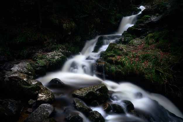 Uma cachoeira poderosa em uma floresta perto de formações rochosas cobertas de musgo