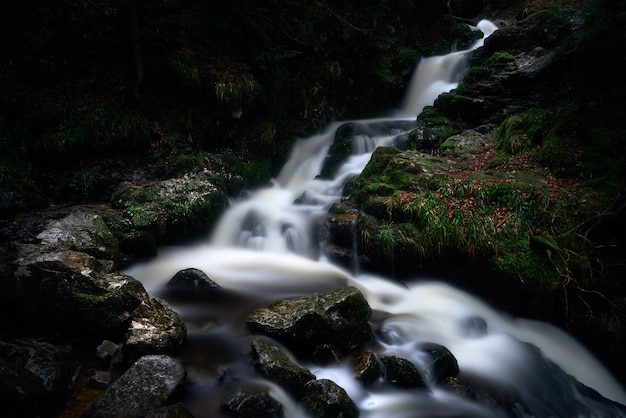 uma cachoeira poderosa em uma floresta perto de formações rochosas cobertas de musgo