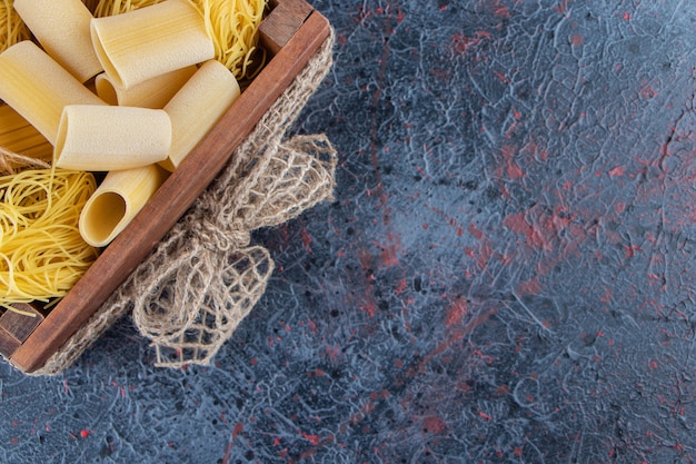 Foto grátis uma caixa de madeira de macarrão cru com tomates vermelhos frescos e alho em um fundo escuro.