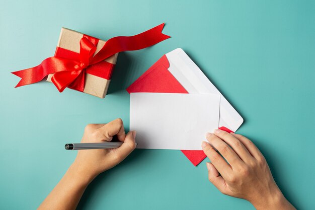 Uma caixa de presente colocada ao lado da mão de uma mulher está escrevendo um cartão de felicitações
