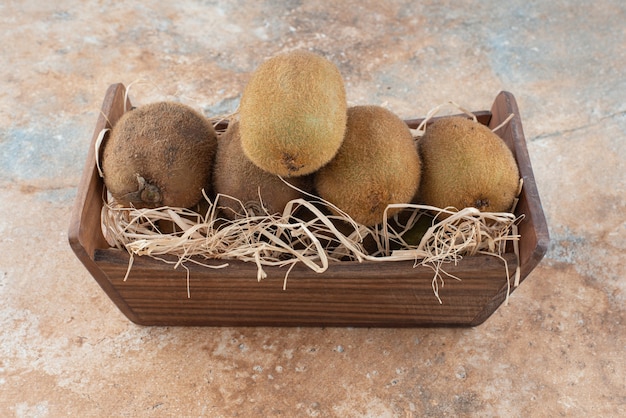 Uma cesta de madeira de kiwi fresco na mesa de mármore.