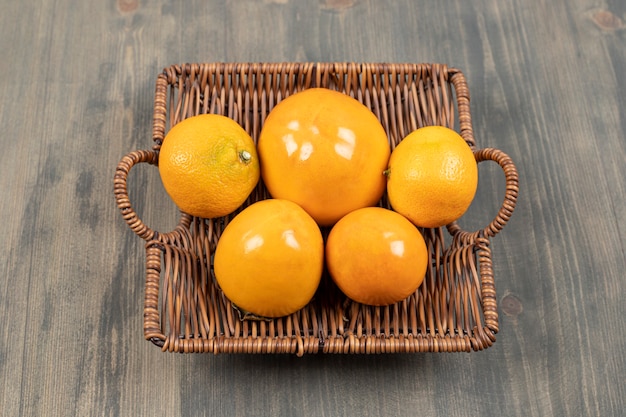 Uma cesta de vime cheia de tangerinas frescas em uma mesa de madeira. foto de alta qualidade