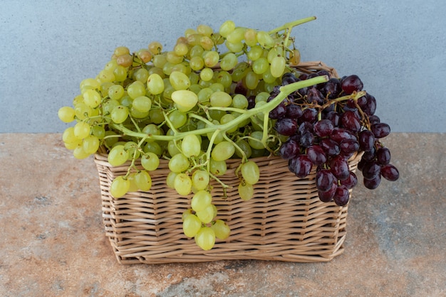 Foto grátis uma cesta de vime cheia de uvas doces na mesa de mármore.