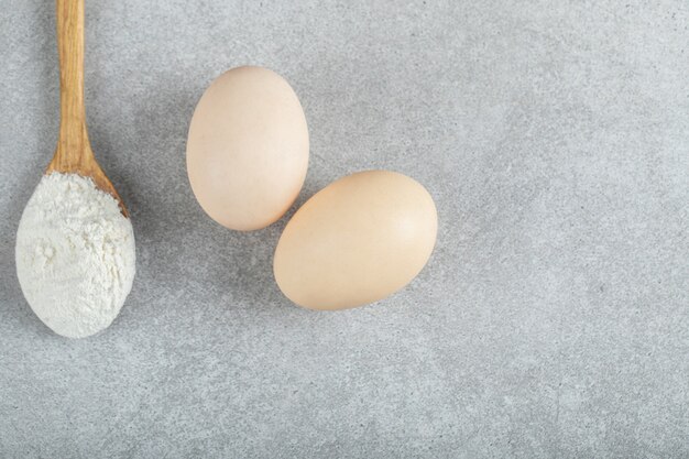 Uma colher de pau com farinha e ovos de galinha.
