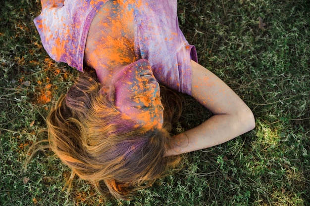 Foto grátis uma cor de holi laranja no rosto da mulher deitada na grama verde