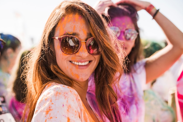 Uma cor de holi laranja no rosto de mulher usando óculos escuros