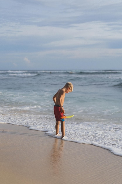 Uma criança na praia brinca nas ondas do oceano. Menino no oceano, infância feliz. vida tropical.